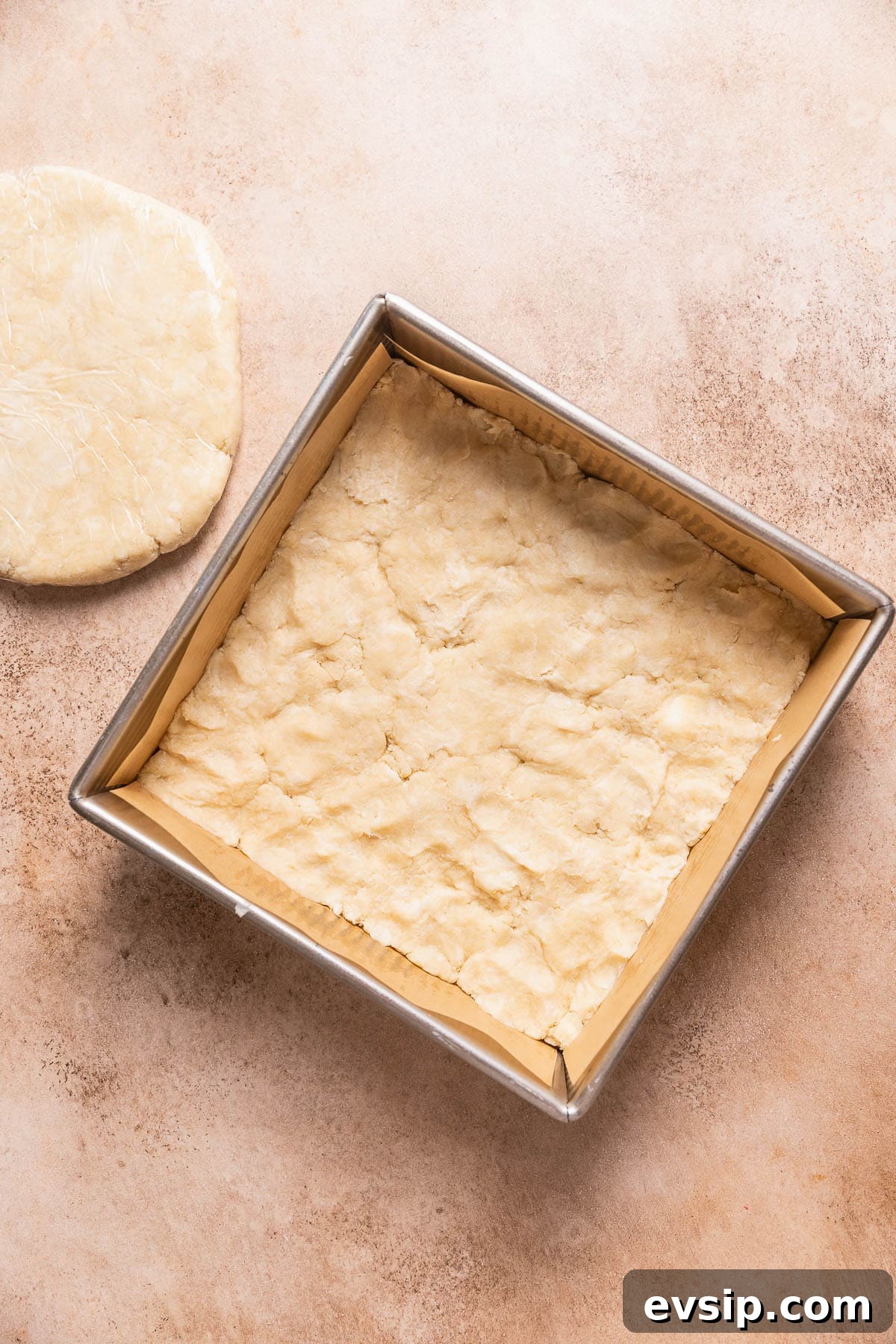 A square baking pan with pie dough pressed into the bottom and a slab of pie dough next to each other.