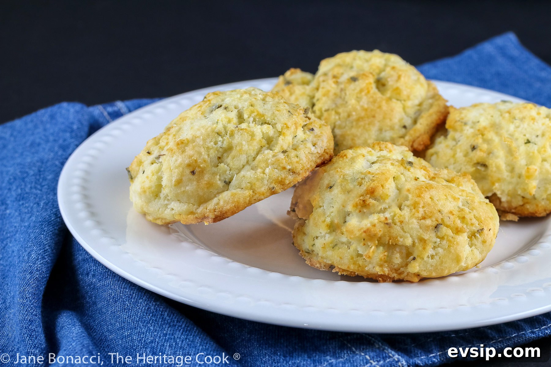 White plate with golden brown drop Easy Cream Biscuits set on a deep blue napkin and black background © 2023 Jane Bonacci, The Heritage Cook.