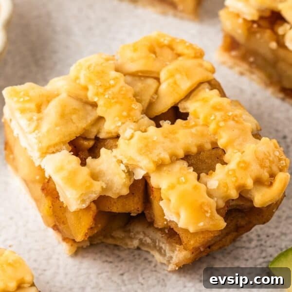 A close-up of delicious Apple Pie Bars, featuring a square slice with a golden-brown lattice crust and sugar sprinkled on top.