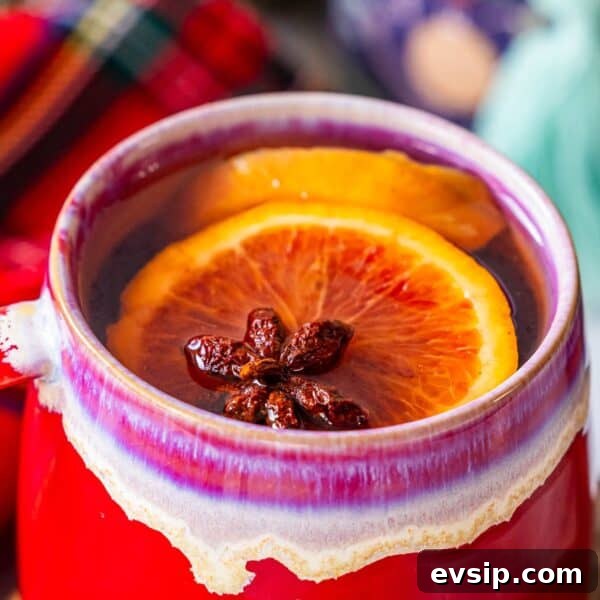 A red mug filled with the Best Mulled Cider Ever, garnished with a slice of orange and star anise.