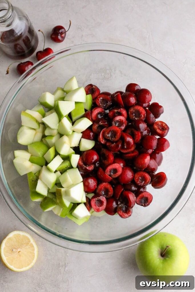 Apple Cherry Tahini Crumble Recipe — Rustic Fruit Dessert 5 sliced cherries and diced apples in bowl with berries and apple and lemon on side