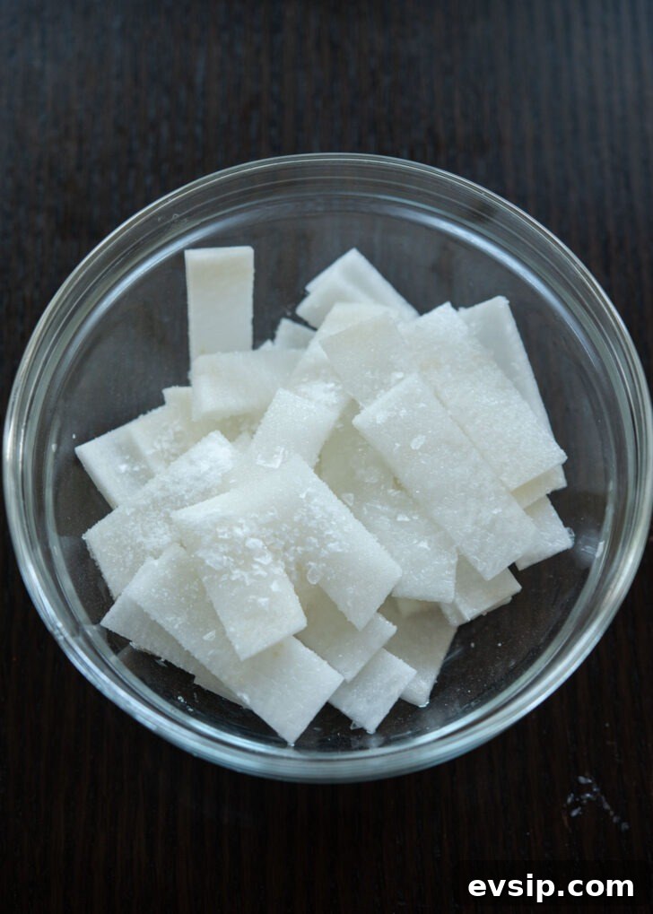 Thinly sliced Korean radish being brined with salt, sugar, and vinegar for a quick pickled topping.
