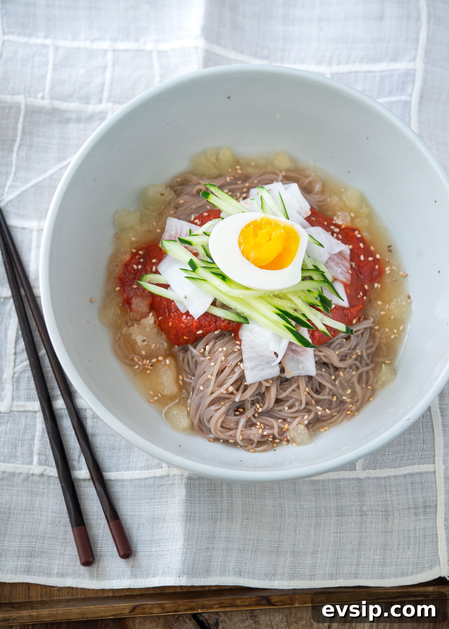 Bibim naengmyeon served in a bowl with spicy sauce, crisp toppings, and a splash of cold beef broth.