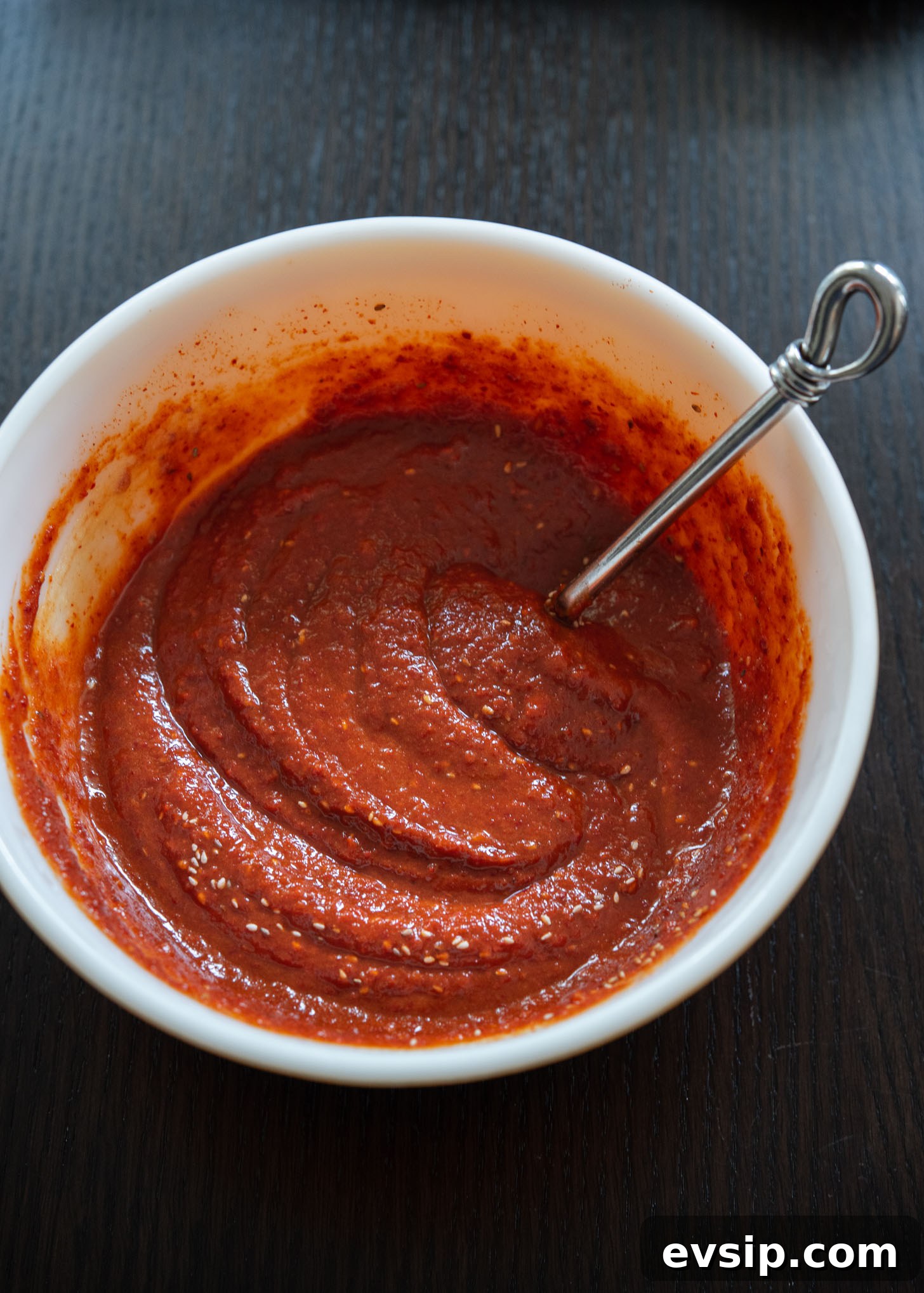 Spicy bibim naengmyeon sauce blended with gochugaru, soy sauce, vinegar, and aromatics in a bowl.