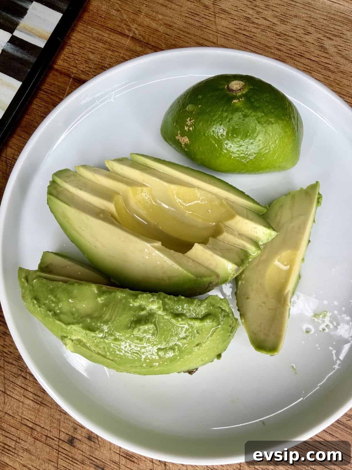 Crispy Mahi Mahi Fish Tacos with Zesty Slaw 12 Sliced avocado drizzled with lemon juice on a white plate, next to half a lime, all placed on a wooden surface.