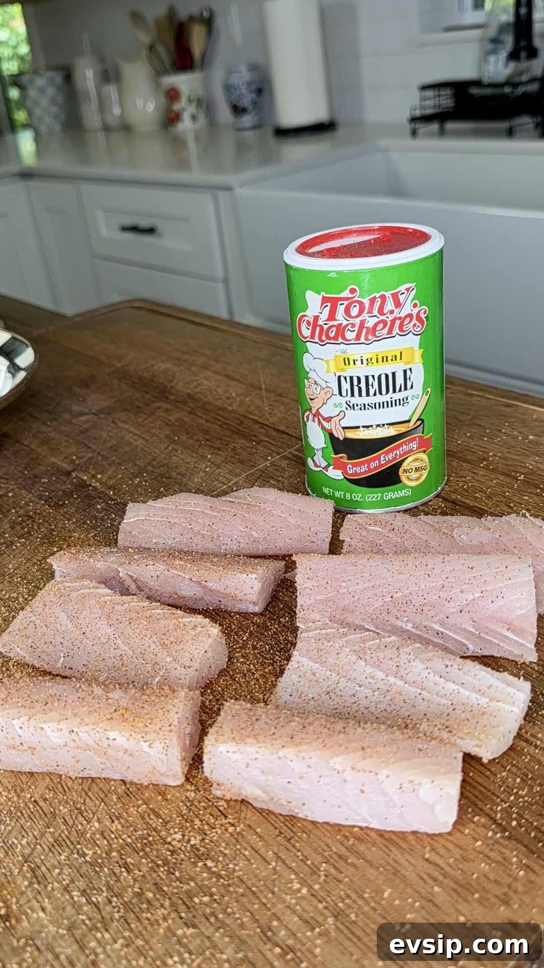 Crispy Mahi Mahi Fish Tacos with Zesty Slaw 4 Raw fish fillets on a wooden cutting board are sprinkled with seasoning. Behind them is a canister of Tony Chachere’s Original Creole Seasoning, set in a bright, white kitchen.