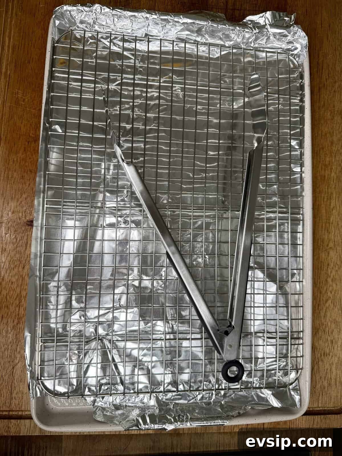 Crispy Mahi Mahi Fish Tacos with Zesty Slaw 5 A baking sheet covered with crumpled aluminum foil, topped with a metal cooling rack. A pair of metal tongs is resting diagonally across the rack. The surface beneath appears to be wooden.