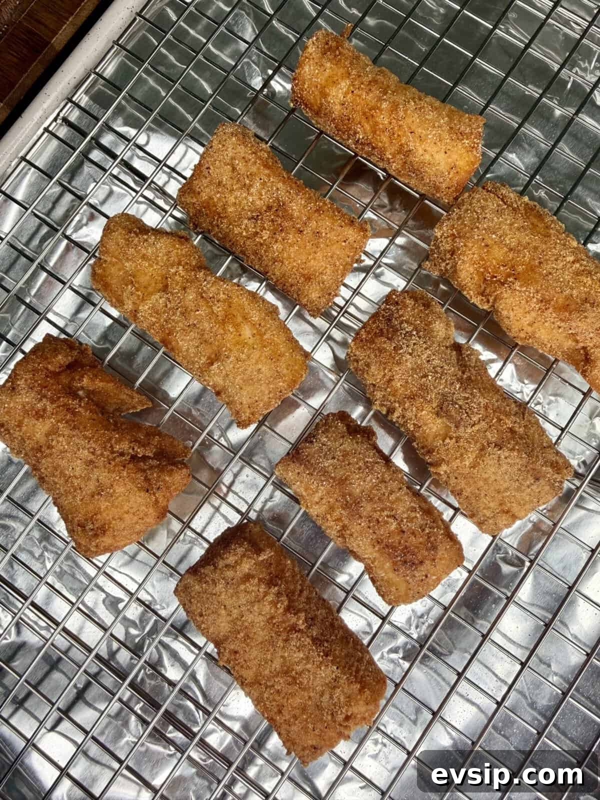Crispy Mahi Mahi Fish Tacos with Zesty Slaw 7 Eight golden-brown, rectangular pieces of food coated in cinnamon sugar rest on a wire cooling rack lined with aluminum foil.
