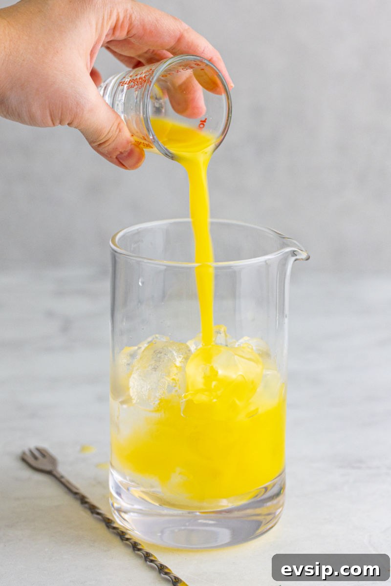 orange juice being poured into a cocktail mixing glass with ice, vodka, and peach schnapps