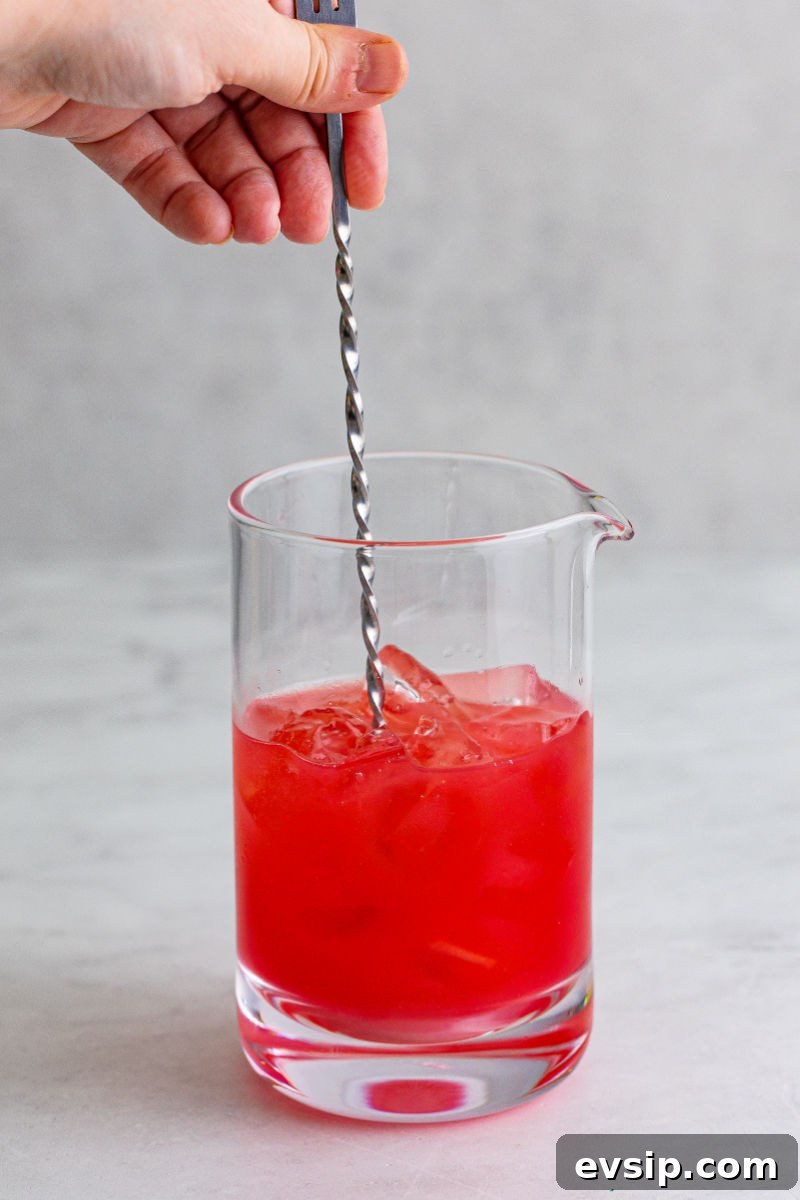bar spoon stirring a sex on the beach cocktail in a mixing glass