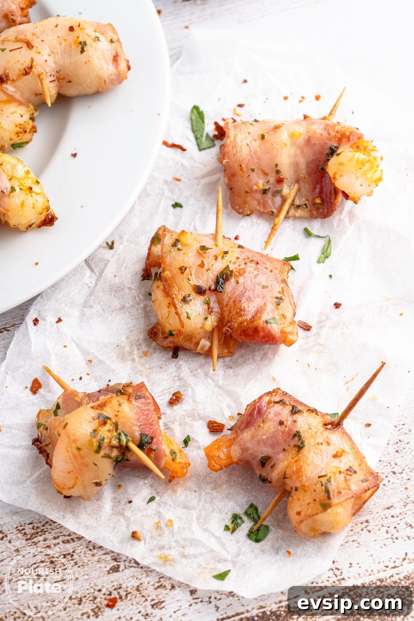 Overhead shot of bacon wrapped shrimp on white parchment paper and a plate on the side