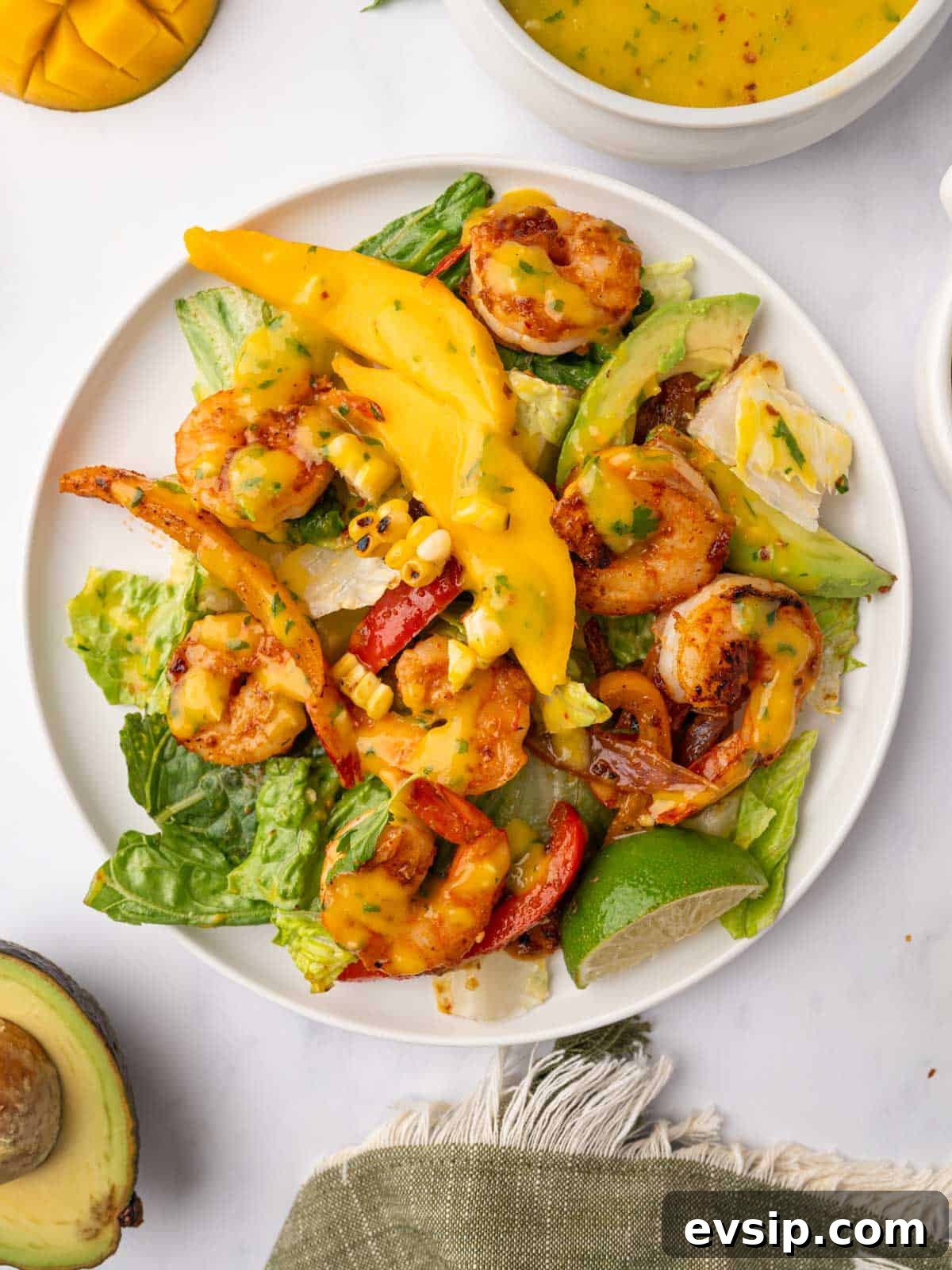 Salad topped with shrimp and mango slices on a plate.