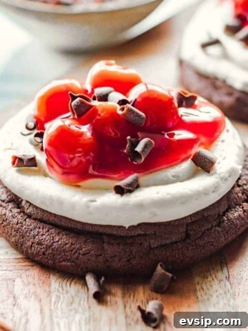 Baked cherry chocolate cheesecake cookie with chocolate shavings on wood board.
