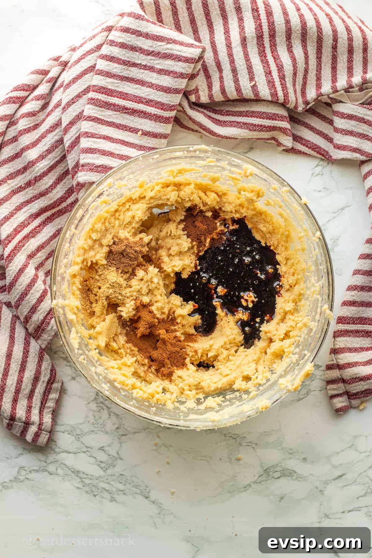 Molasses and spices in butter, sugar, and eggs mixture in glass bowl.
