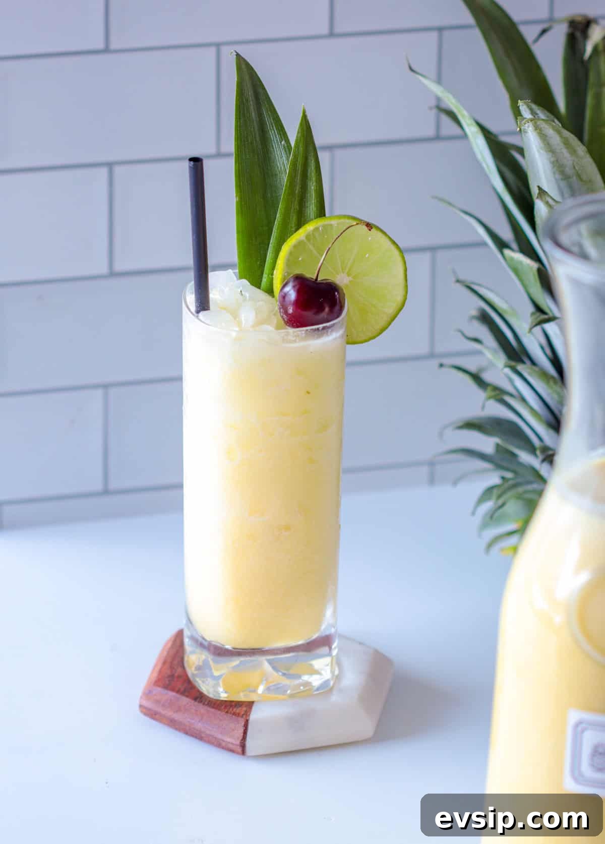 Shaken pina colada over ice with a straw and cherry.