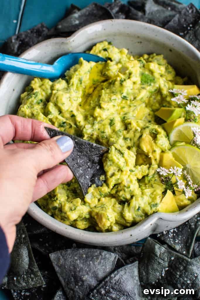 A bowl of guacamole with a hand reaching in with a chip to scoop some up. 
