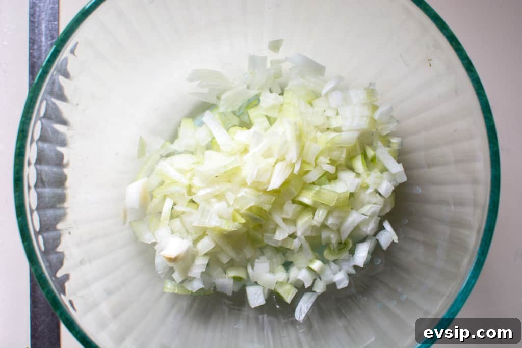 A glass bowl with chopped white onion in it on a white counter. 