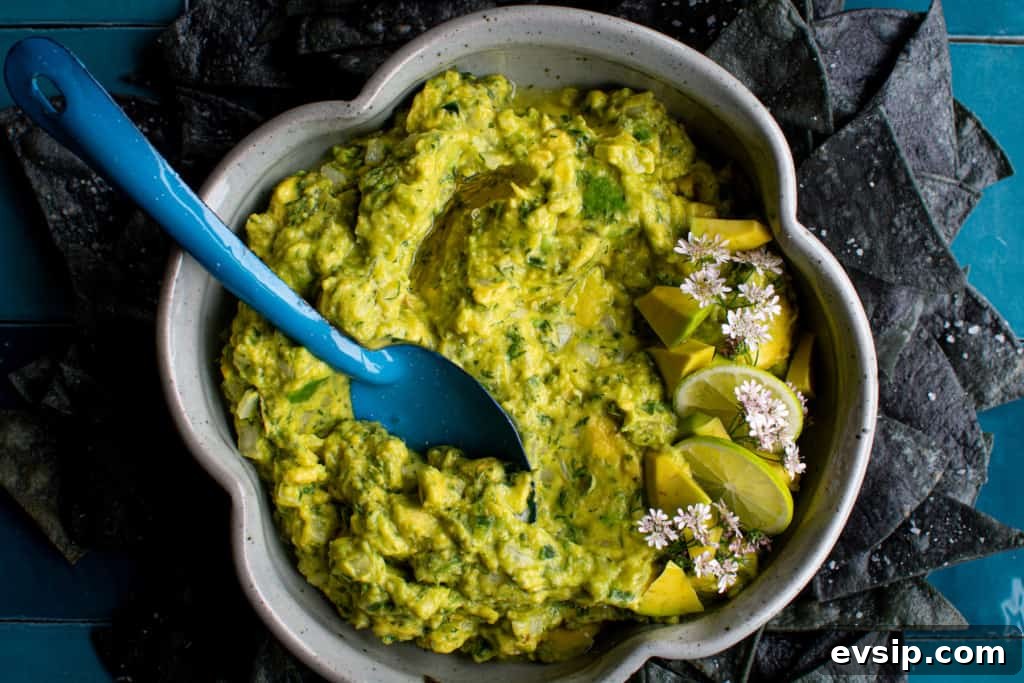 A bowl of guacamole with a blue spoon sticking out of one side and a bunch of blue corn chips surrounding the bowl. 
