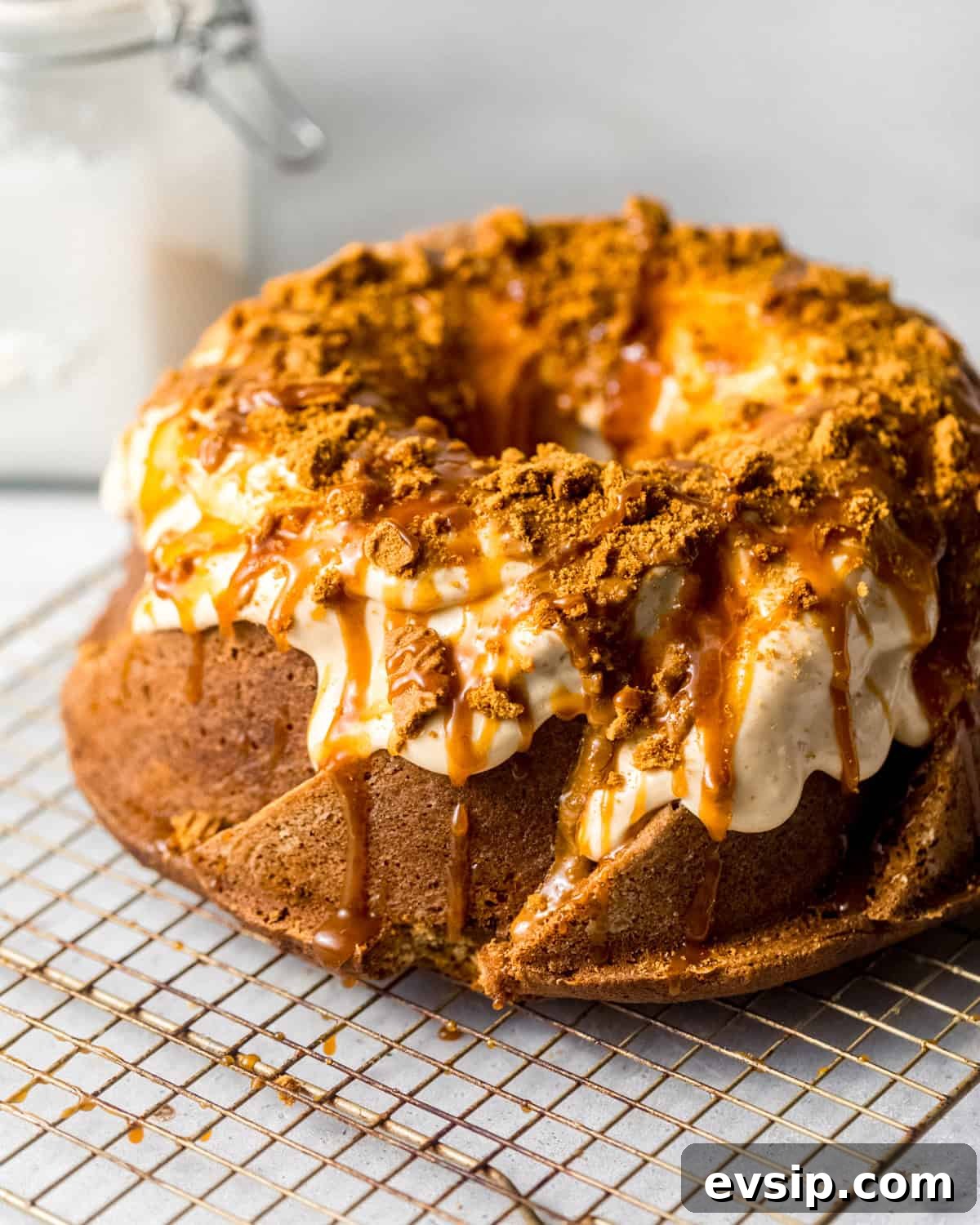 cookie butter cake on a wire rack topped with salted caramel, biscoff cream cheese glaze, and crushed biscoff cookies.
