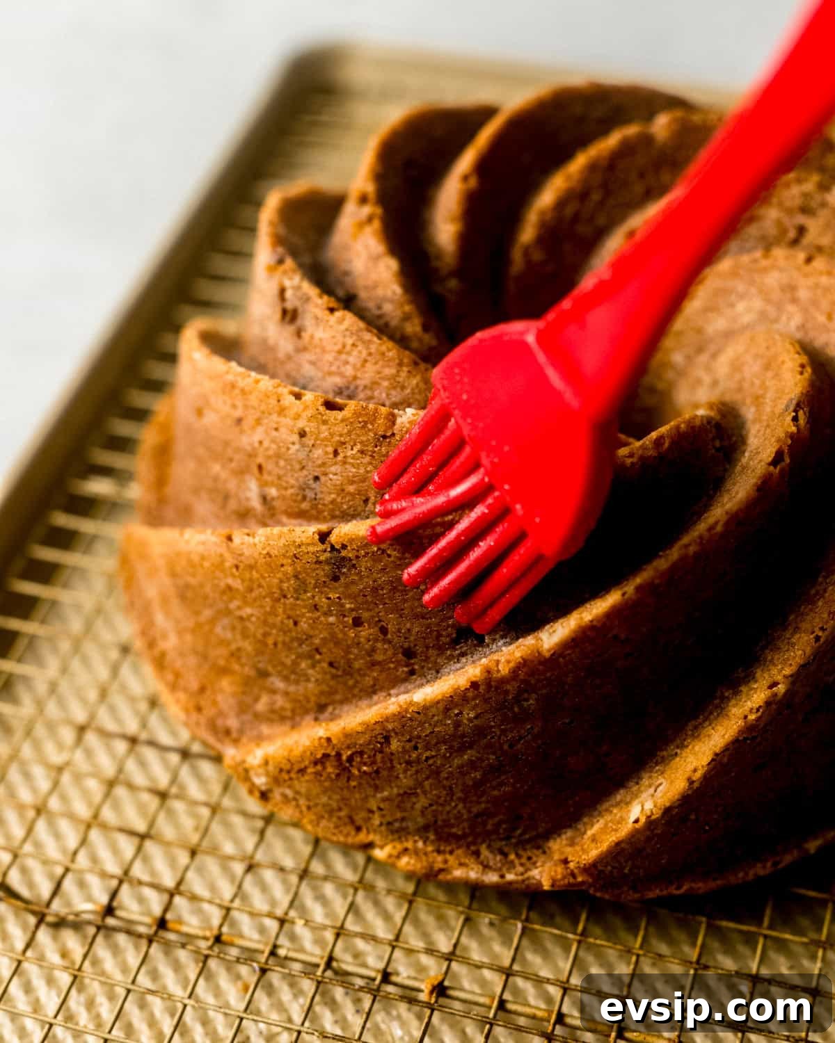 a pastry brush brushing vanilla bean simple syrup onto the biscoff cake.