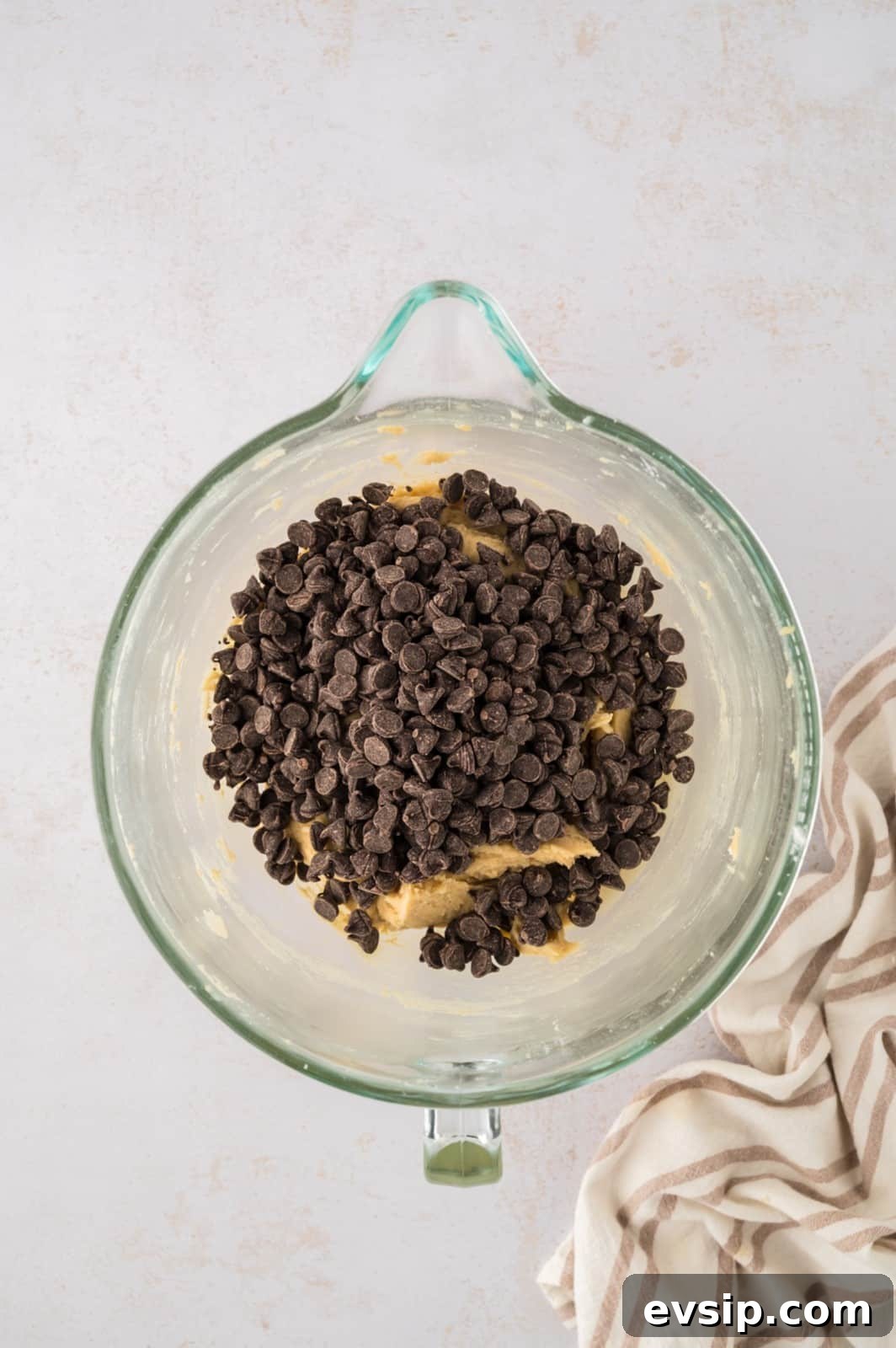 Chocolate chips added to cookie dough in a glass mixing bowl.
