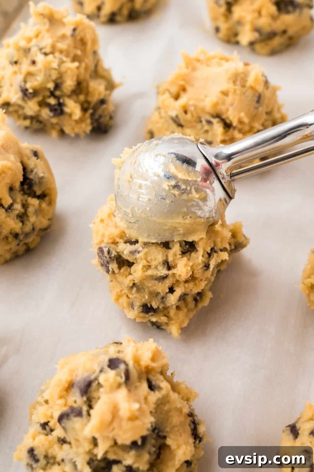 Scooping chocolate chip cookie dough onto a parchment lined baking sheet.