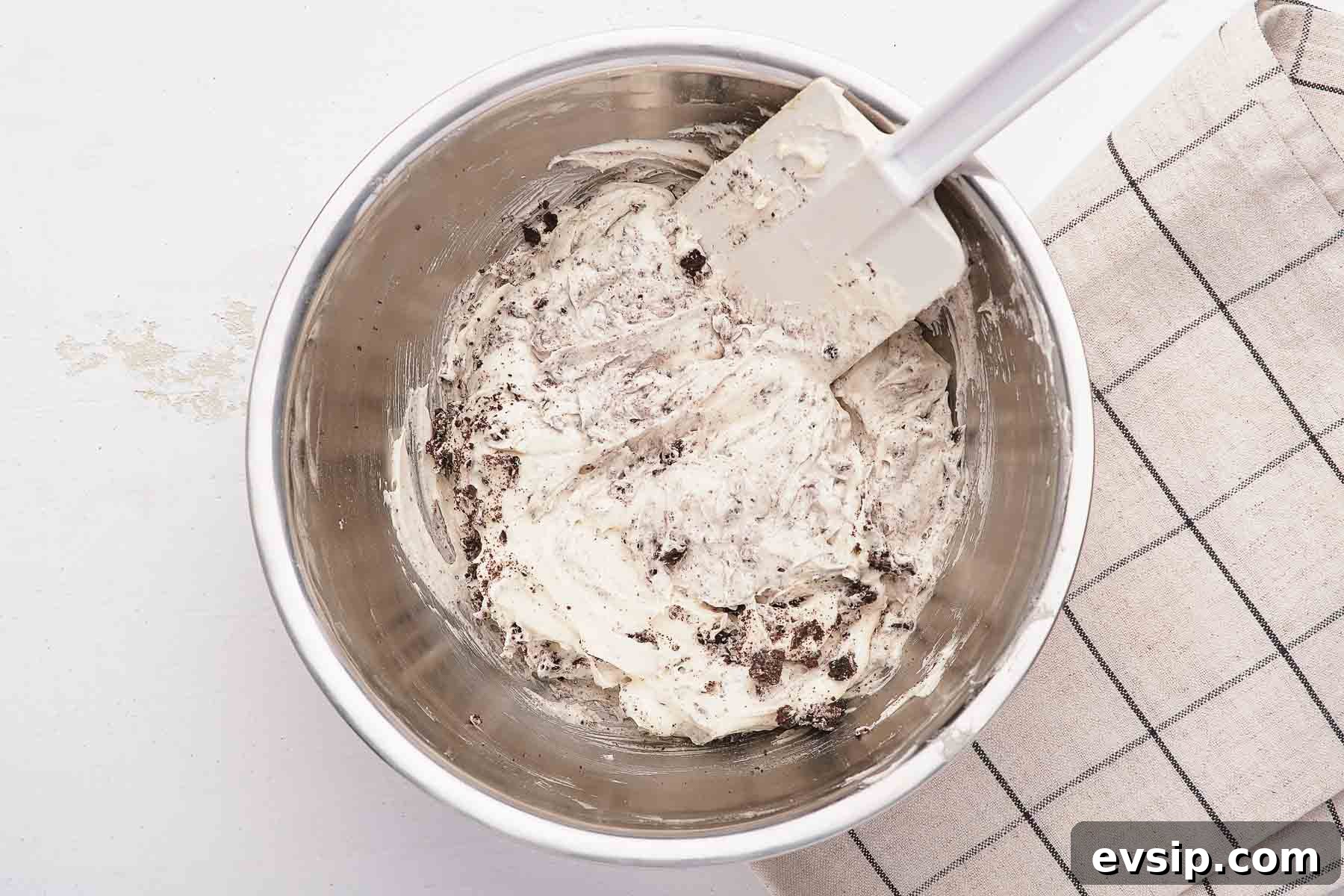 Stirring crushed cookies into white fluffy dessert with spatula.