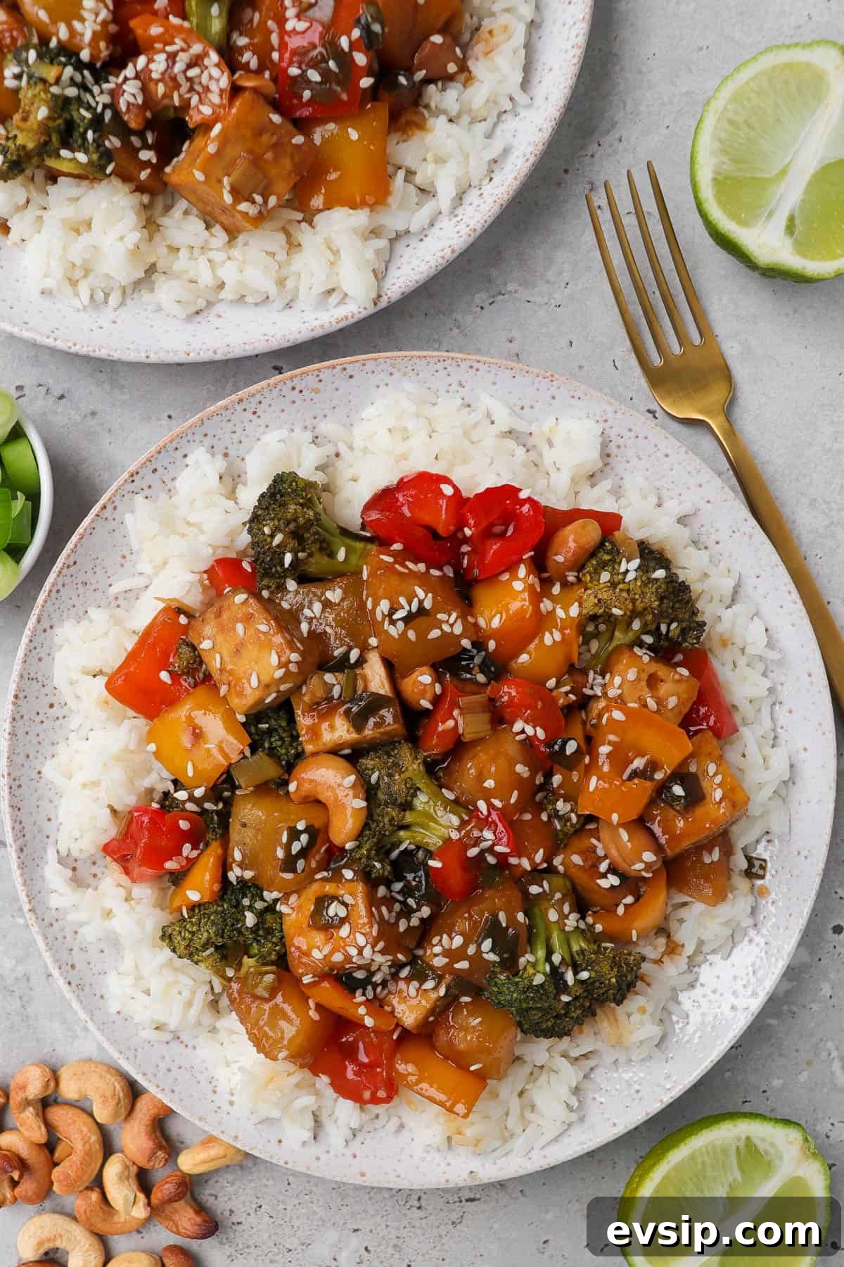 Pienapple tofu served on plate with rice and fork. Roasted cashews, limes and spring onions on sides.