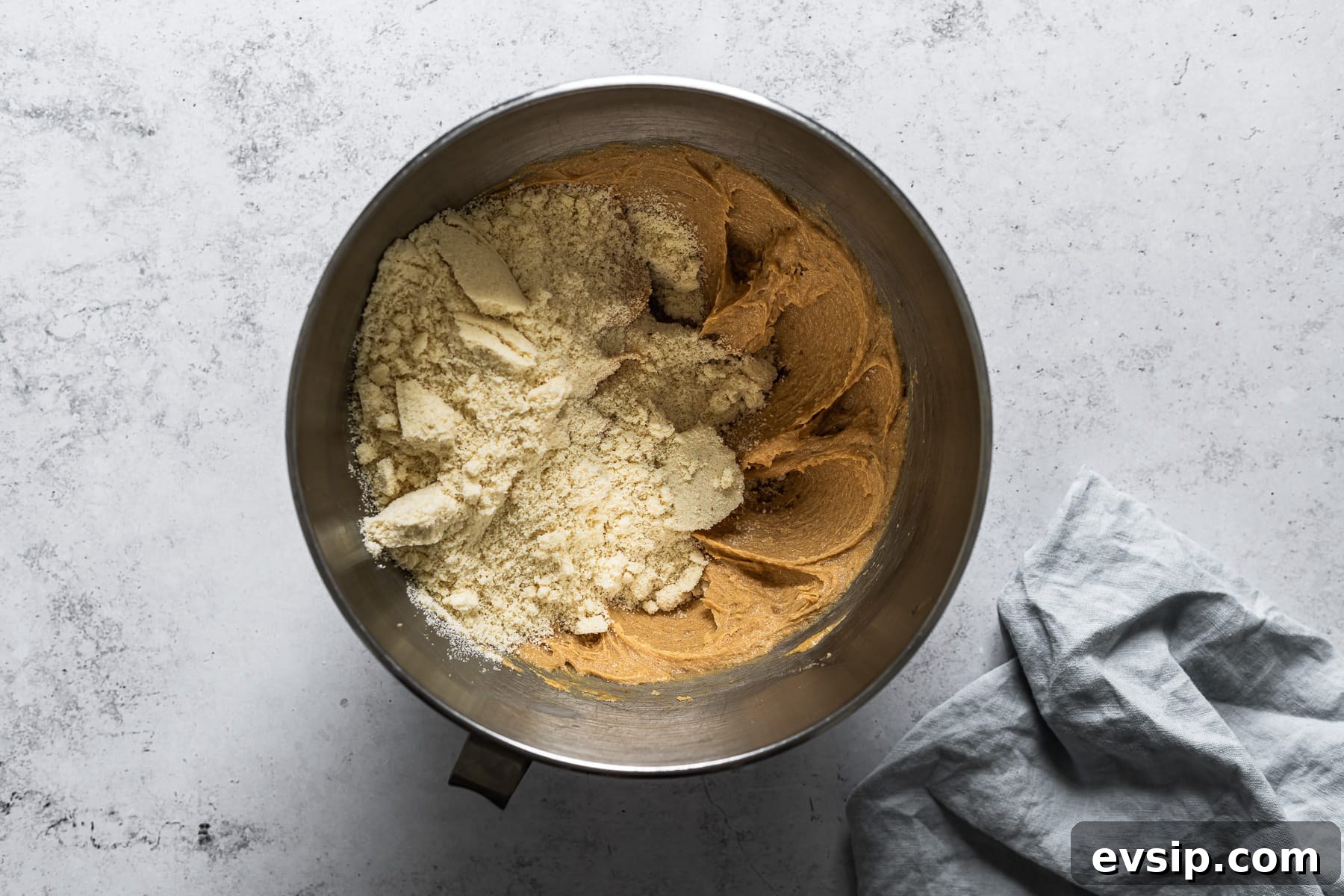 A process photo showing dry ingredients added to a mixing bowl of cookie batter.