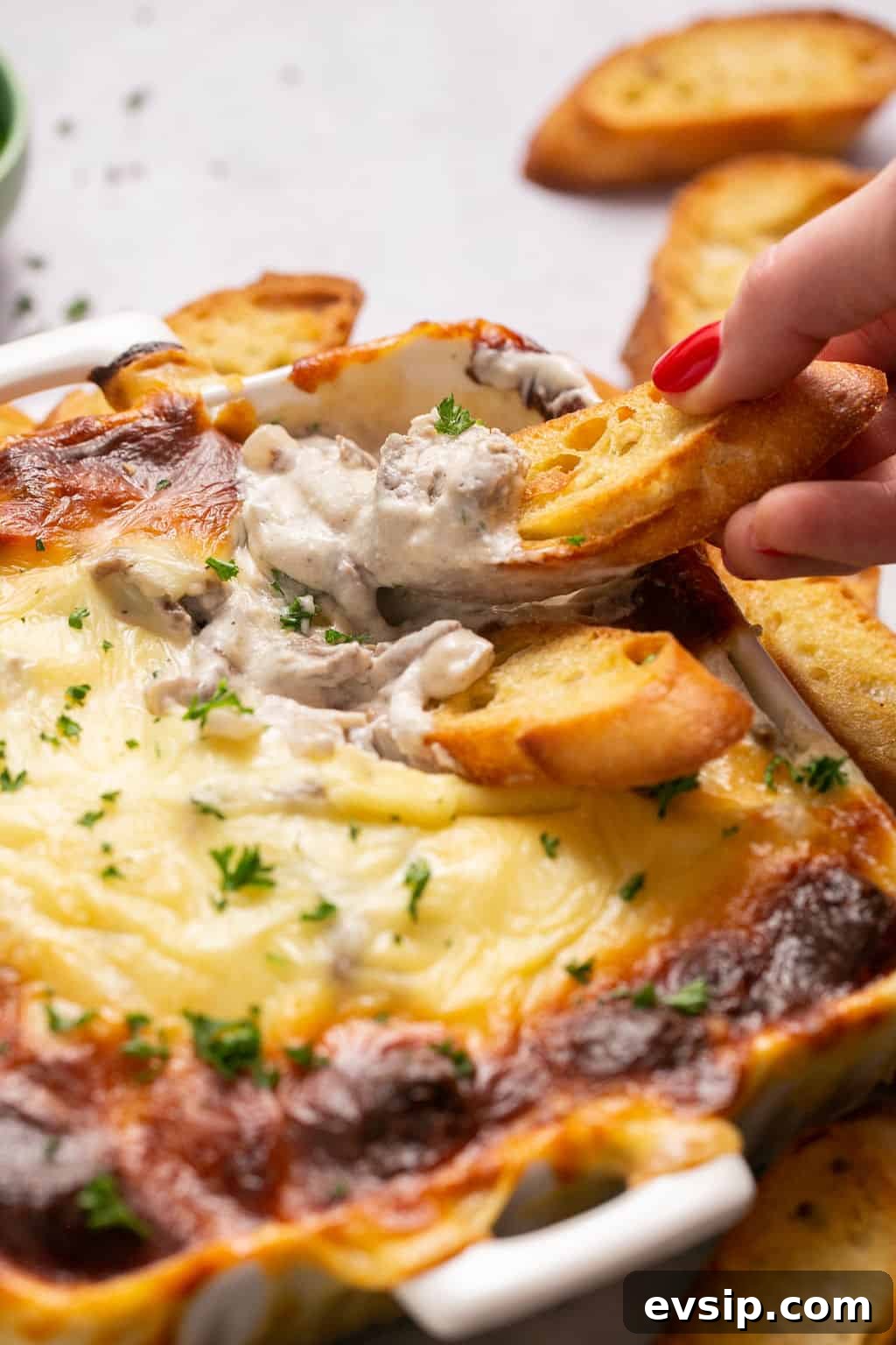 dipping a piece of bread into the Philly cheesesteak dip
