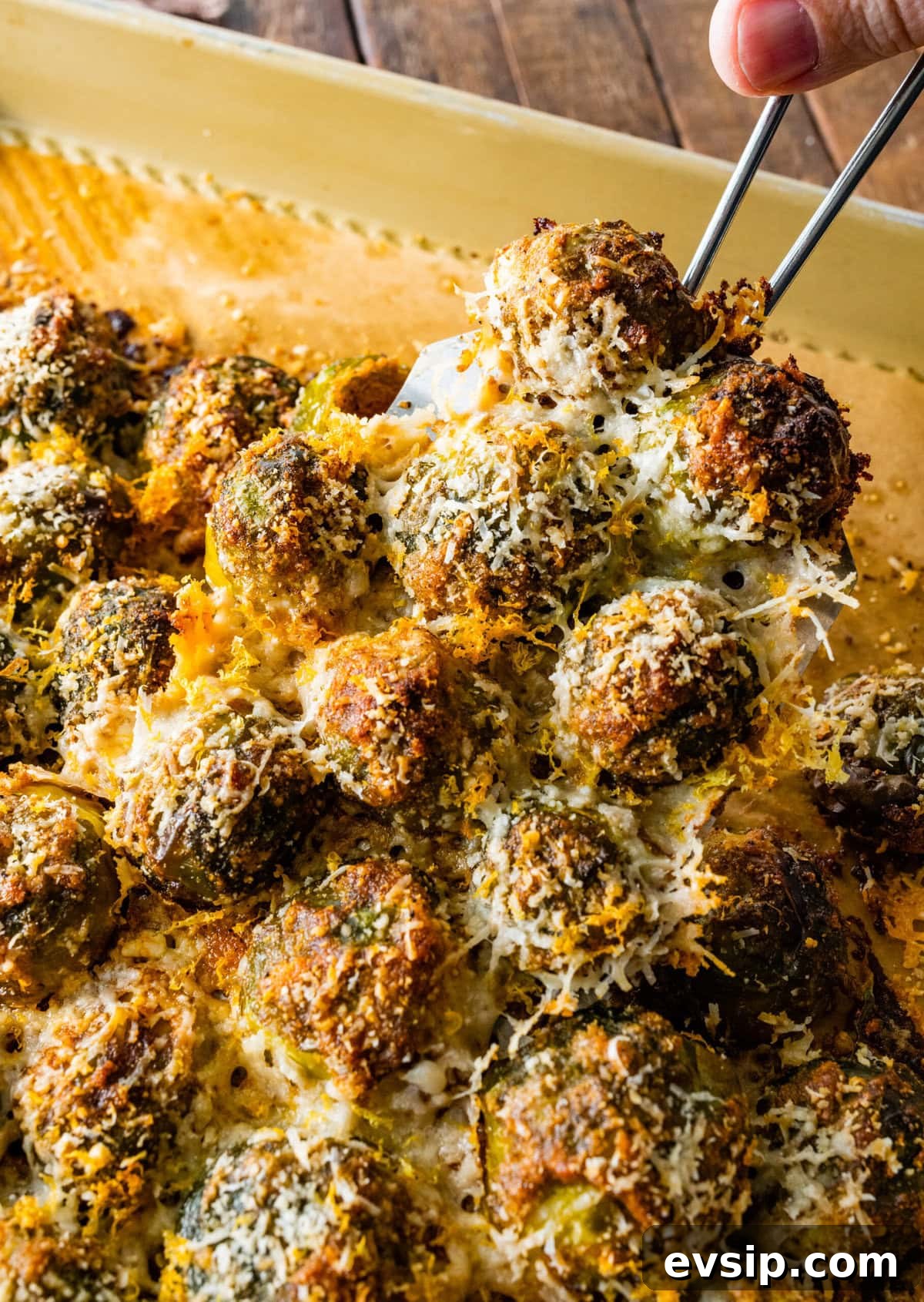 Brussels sprouts after they are baked with a cheesy topping. Spatula lifting up the Brussels Sprouts.