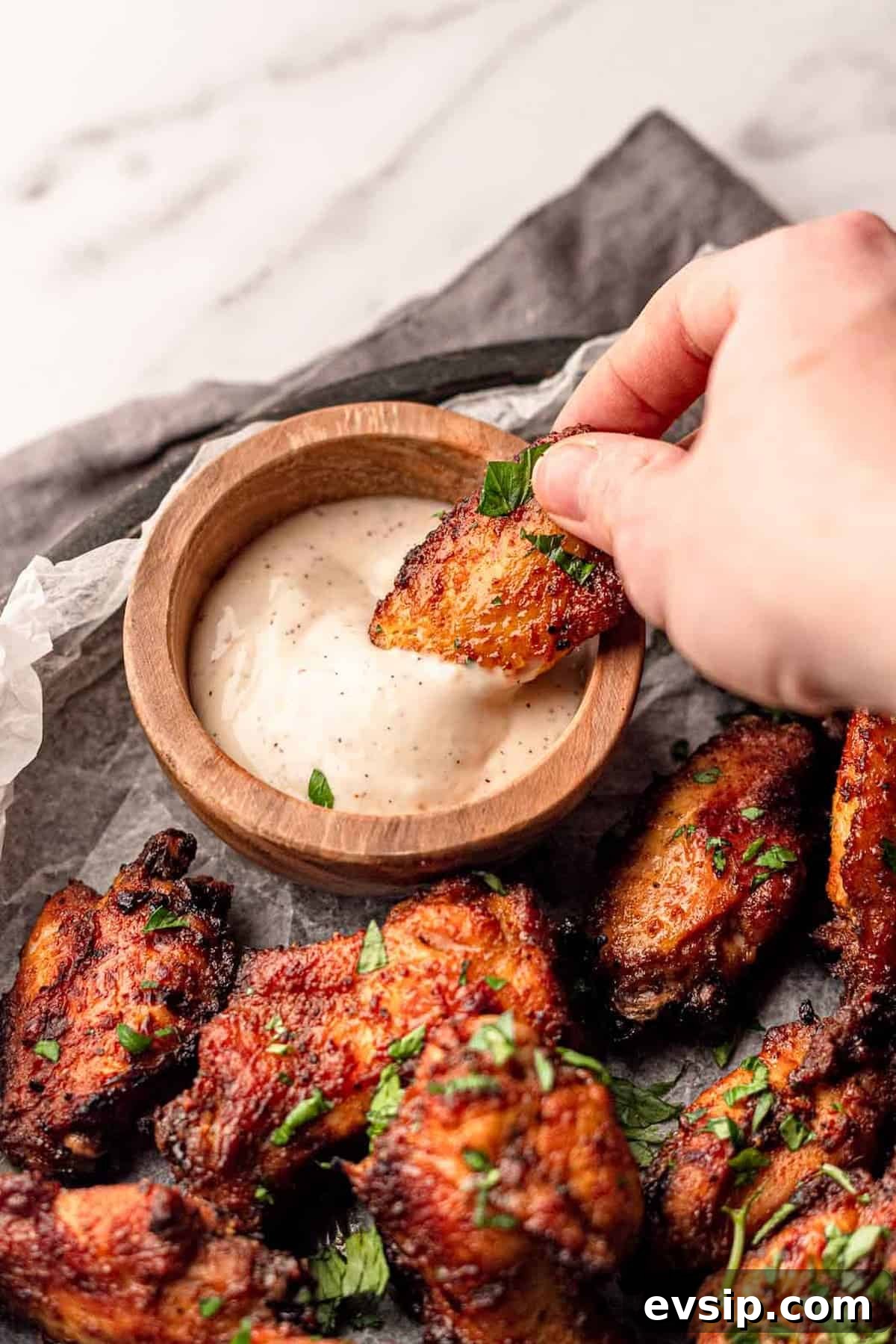 A hand dipping a wing into blue cheese dressing.