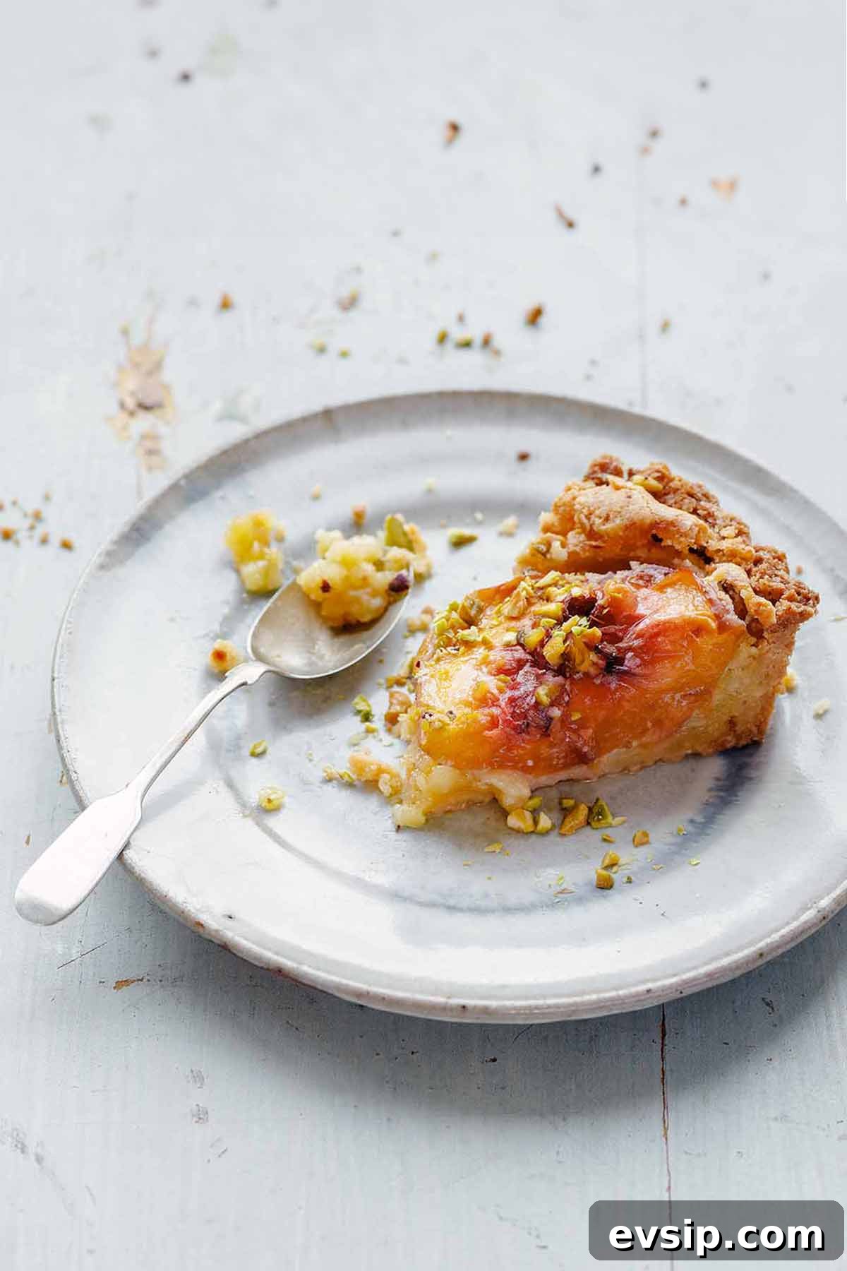 Plate with an slice of apricot tart filled with frangipane and topped with chopped pistachios.