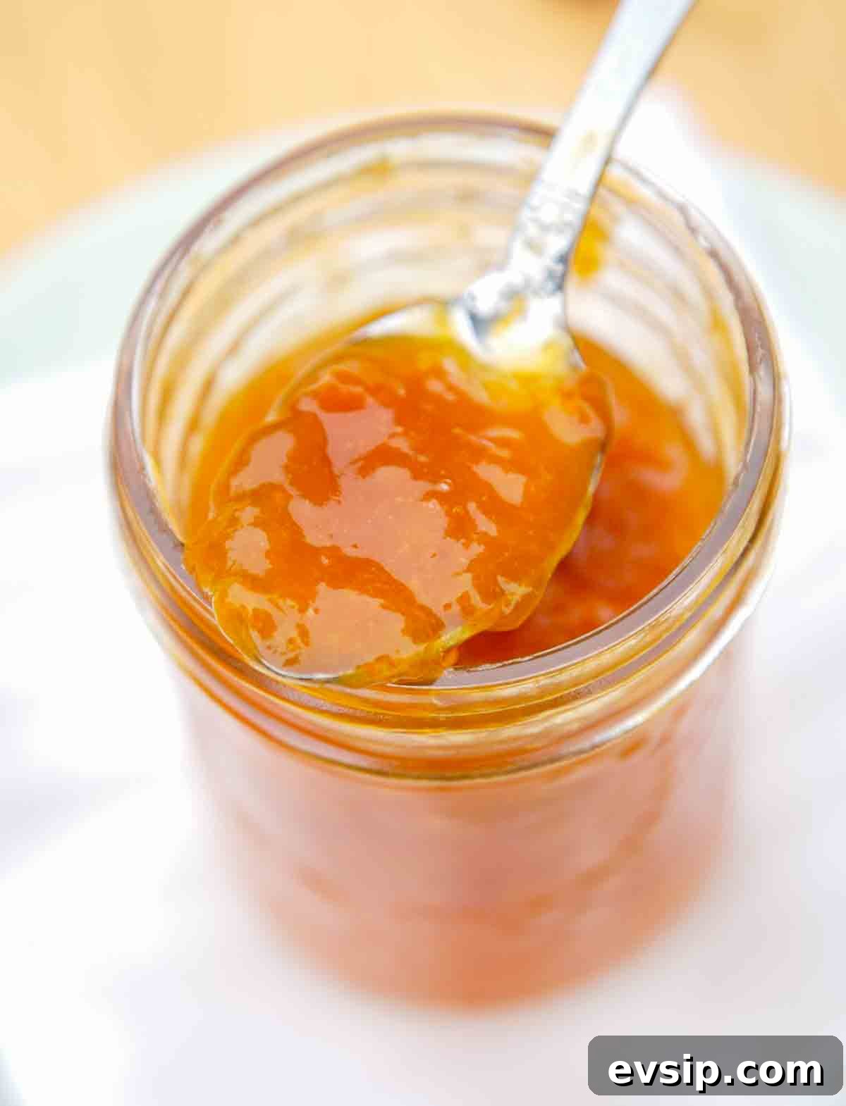 A jelly jar filled with apricot jam and a spoon resting on top.