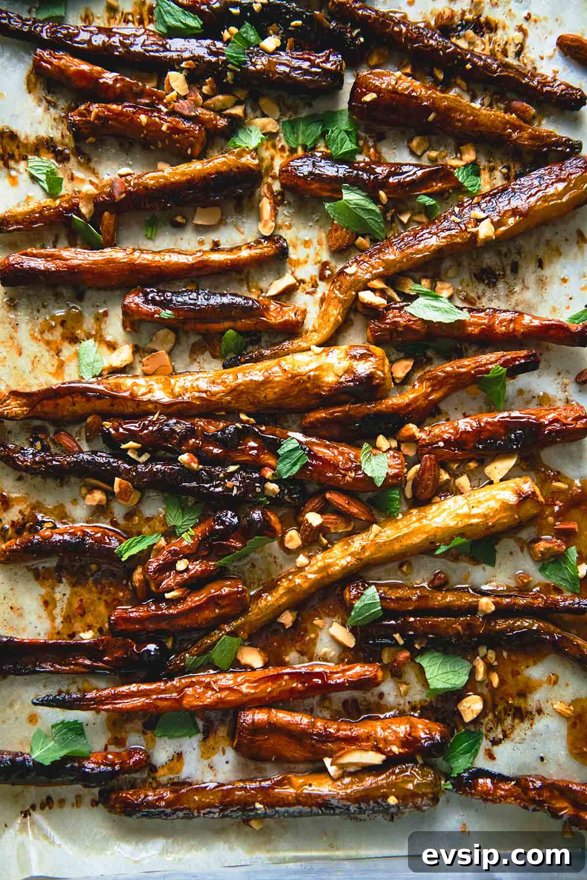 A rimmed baking sheet filled with roasted carrots with apricot glaze, chopped almonds, and torn mint.