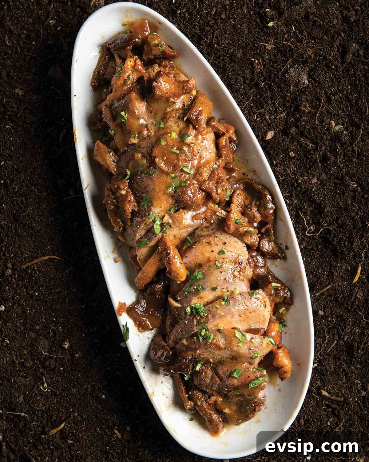 An oval platter containing sliced pork with chanterelles and apricot jam sauce
