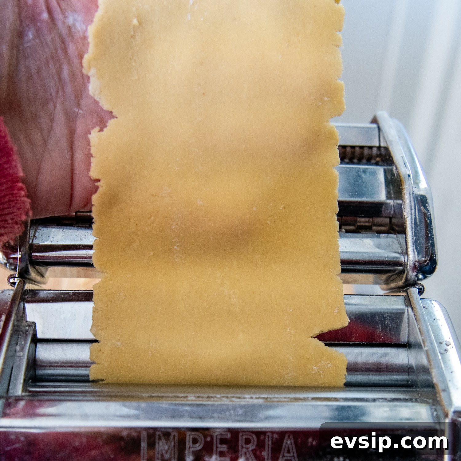dough being flattened by pasta making machine.