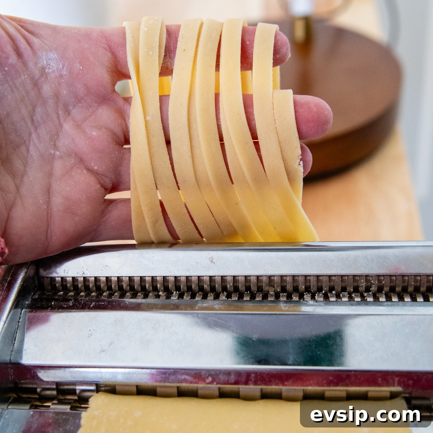 Dough coming out of a pasta maker in fettuccine shape.