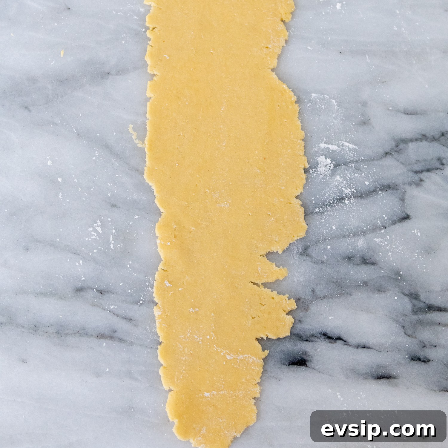 Dough flattened with ragged edges laying on a marble surface.