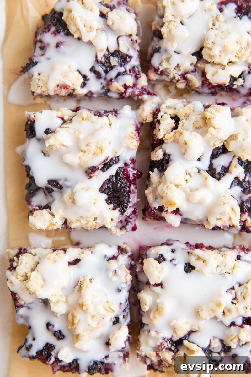 Gluten-Free Vegan Blackberry Pie Bars — 5 Ingredients 12 slices of blackberry crumb bars on parchment paper with glaze drizzled on top.
