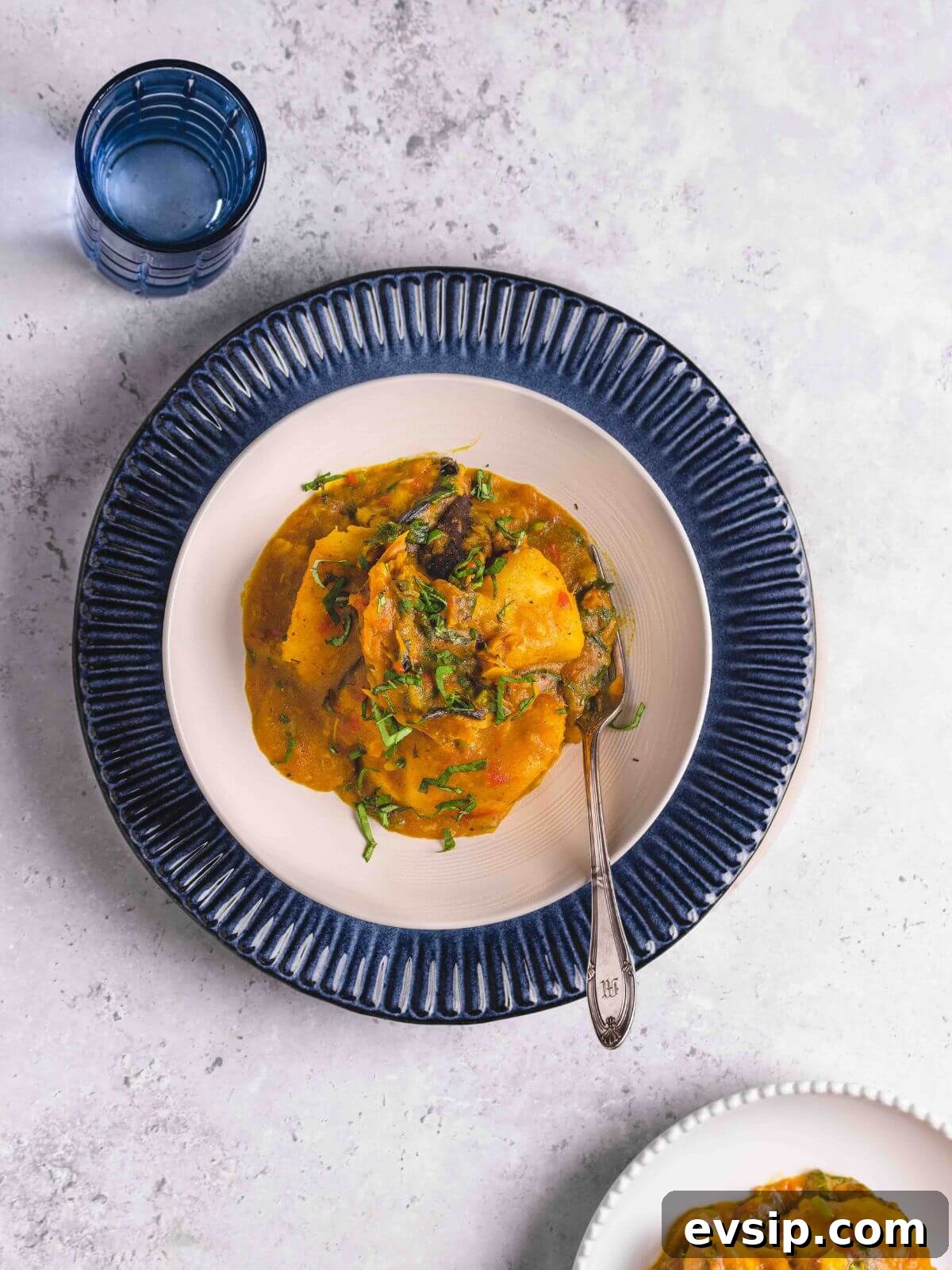 A serving of porridge yam in a white bowl with a glass of water.