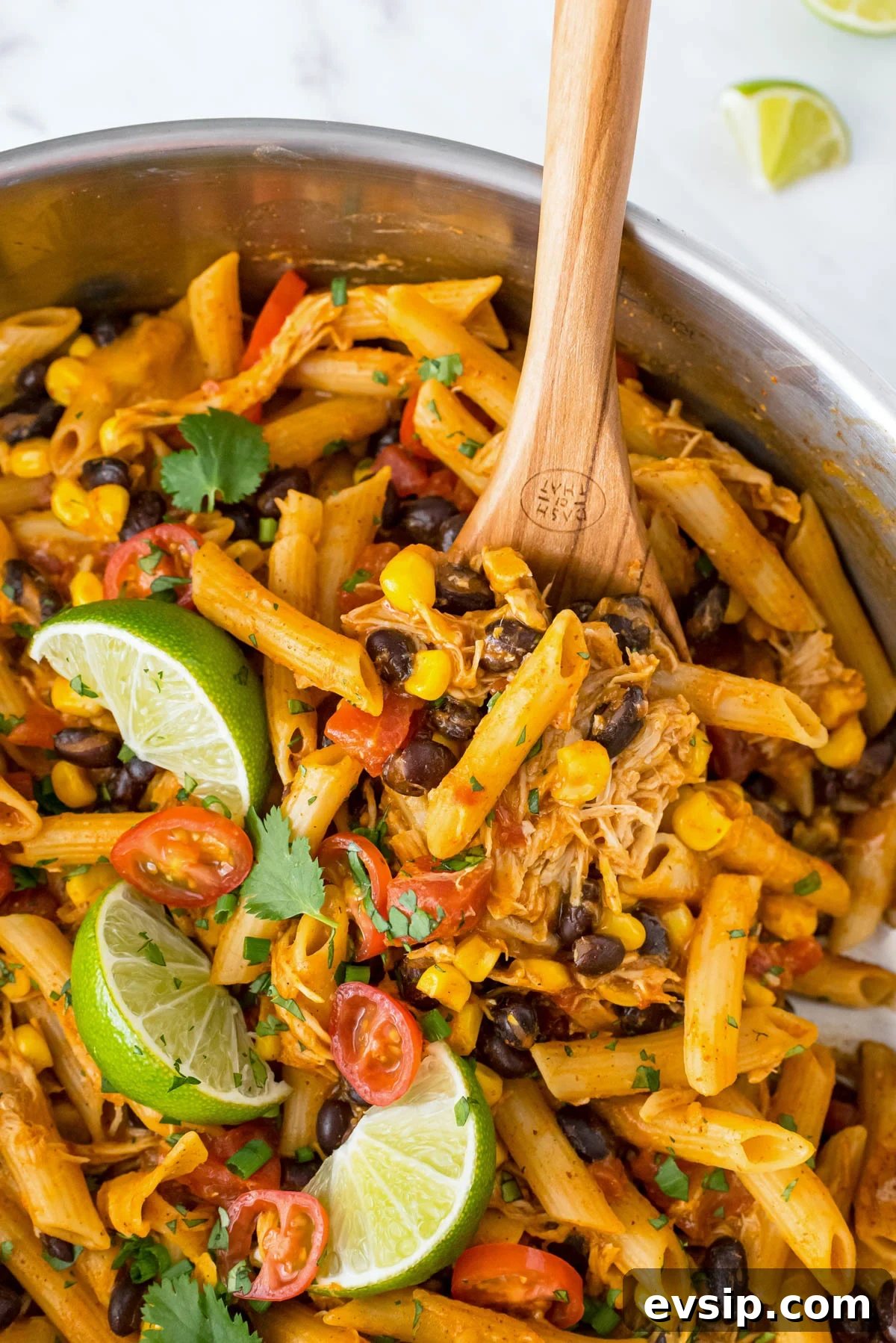 30-Minute One-Pot Chicken Enchilada Pasta Recipe 2 Close up of chicken enchilada pasta with shredded chicken, black beans, corn and enchilada sauce being stirred in a skillet