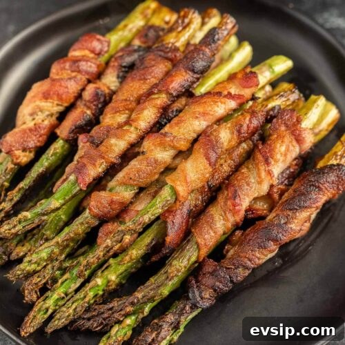 Top Blackstone Griddle Appetizers for Parties and Game Day 19 Bacon wrapped asparagus on a black plate.