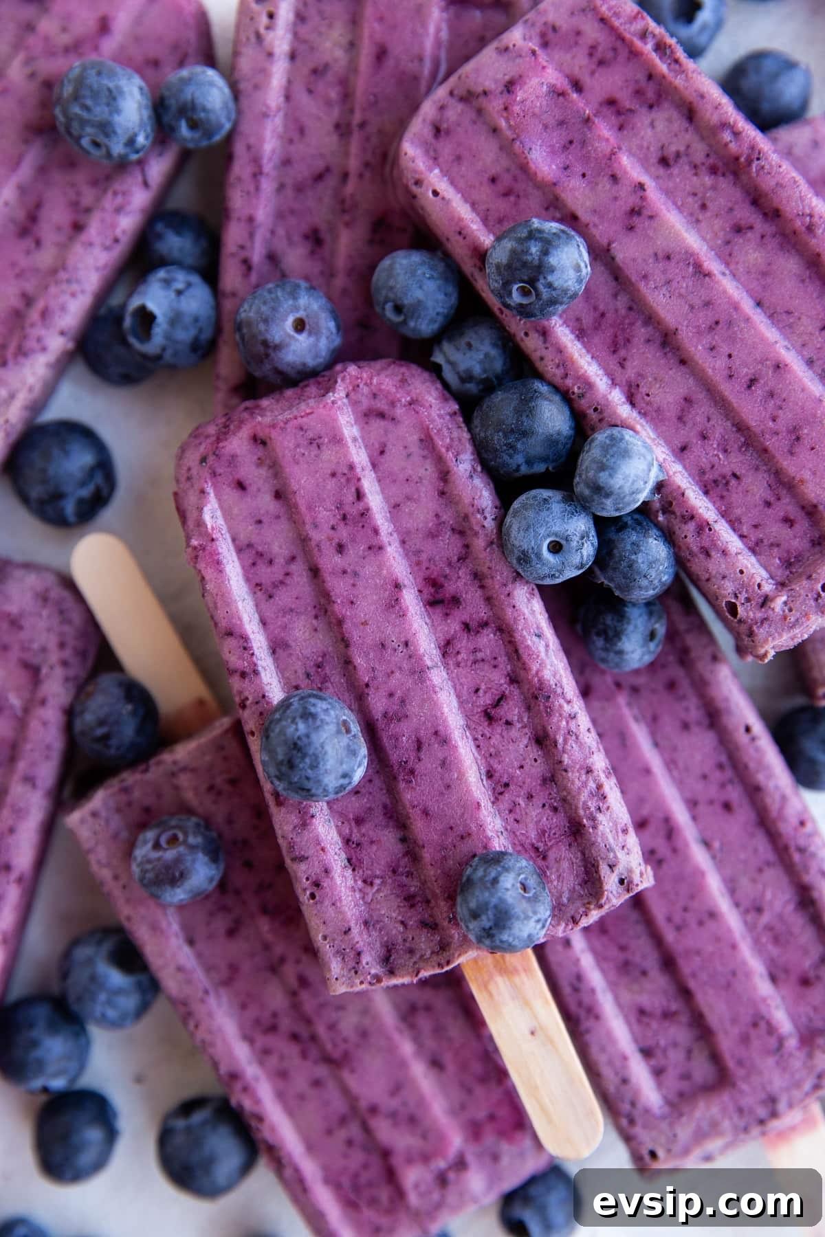 Stack of blueberry coconut milk popsicles with fresh blueberries all around.