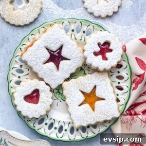 A plate of classic linzer cookies with powdered sugar on top, each featuring a unique cut-out shape that reveals colorful jam.