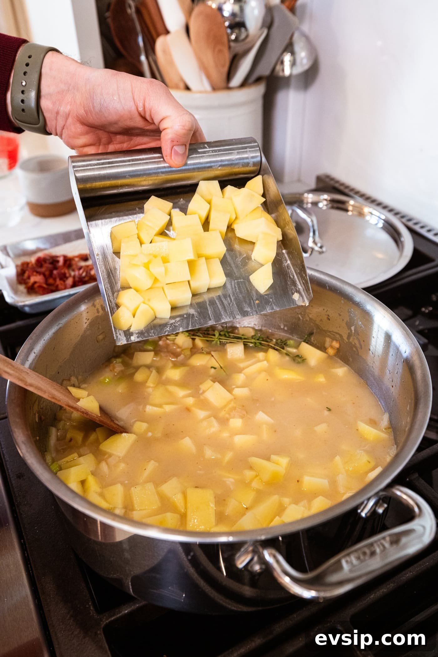 Hand using a scraper to add chopped pieces of potato to a large stockpot already filled with liquid for soup.