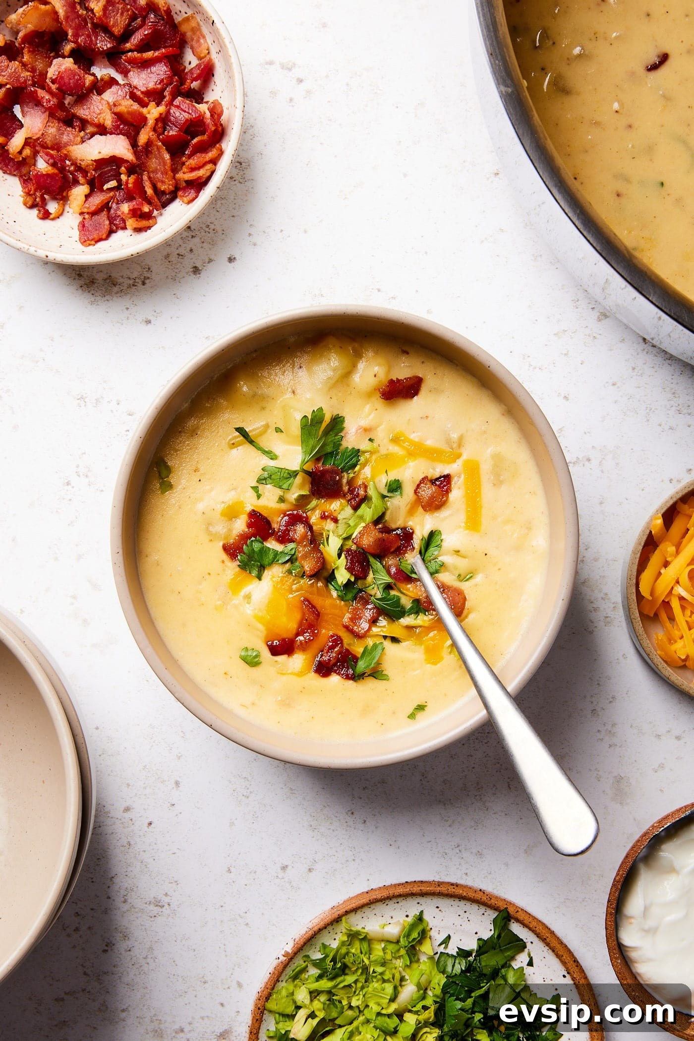 Bowl filled with serving of loaded baked potato soup with bacon and cheese sprinkled on top with rest of toppings on surface.
