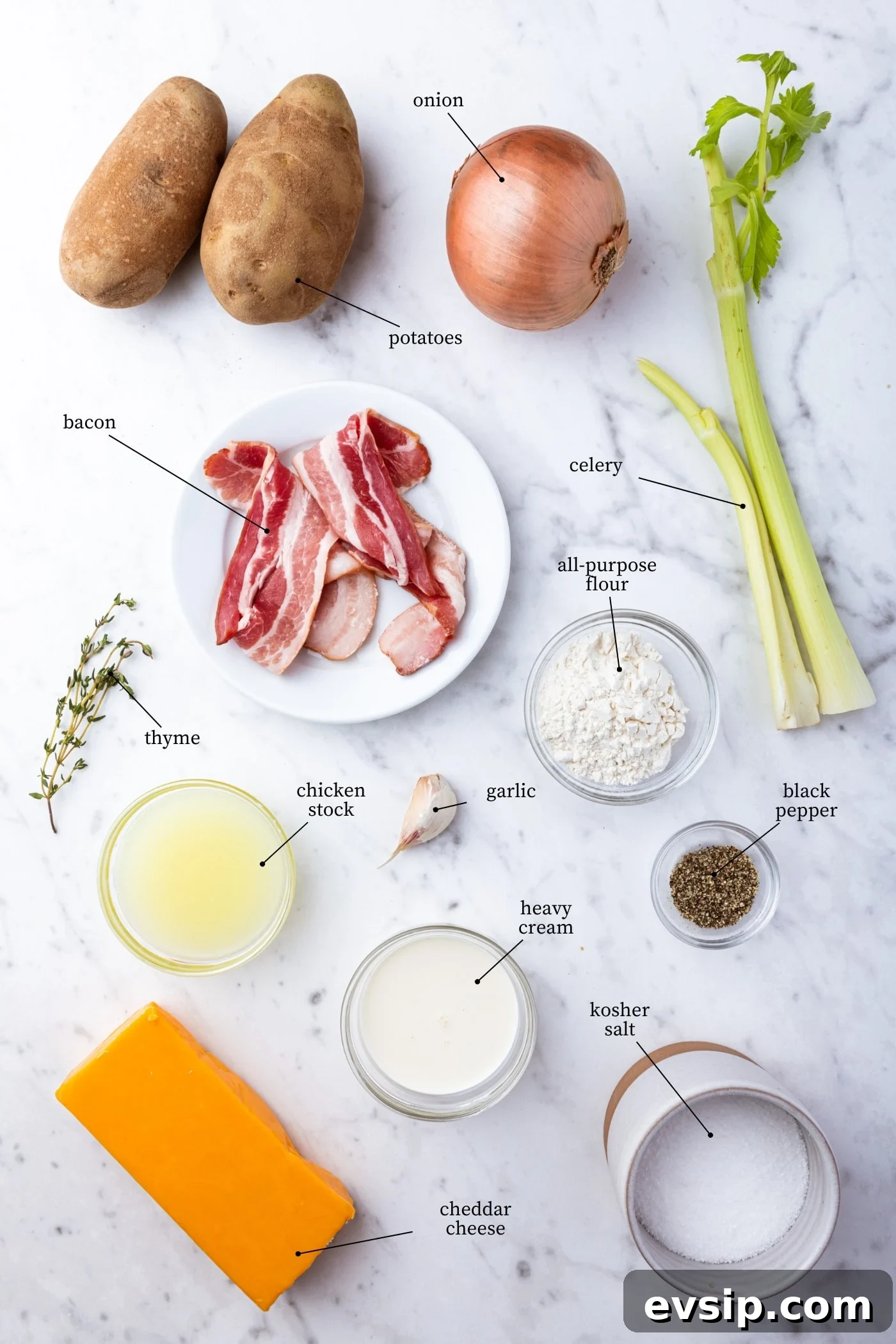 White marble surface with all ingredients needed to make baked potato soup including potatoes, onion, celery, bacon, spices, and more.