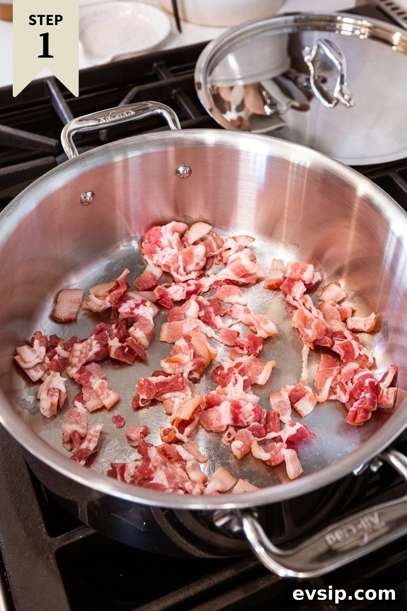 Large metal pan filled with uncooked bacon in oil ready to be cooked until browned.