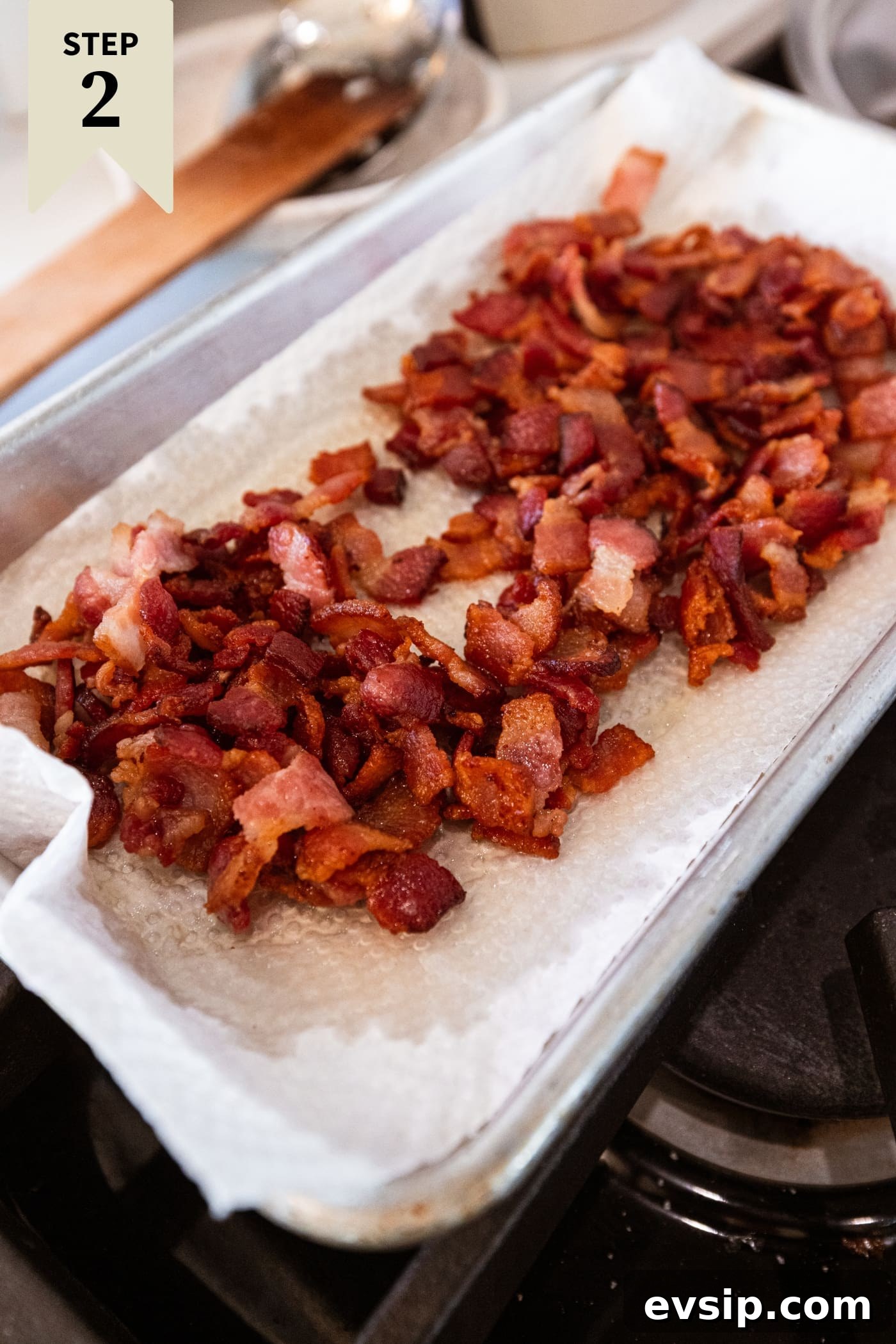Cooked bacon resting on a paper towel-lined small pan after being cooked on the heat on the stove.
